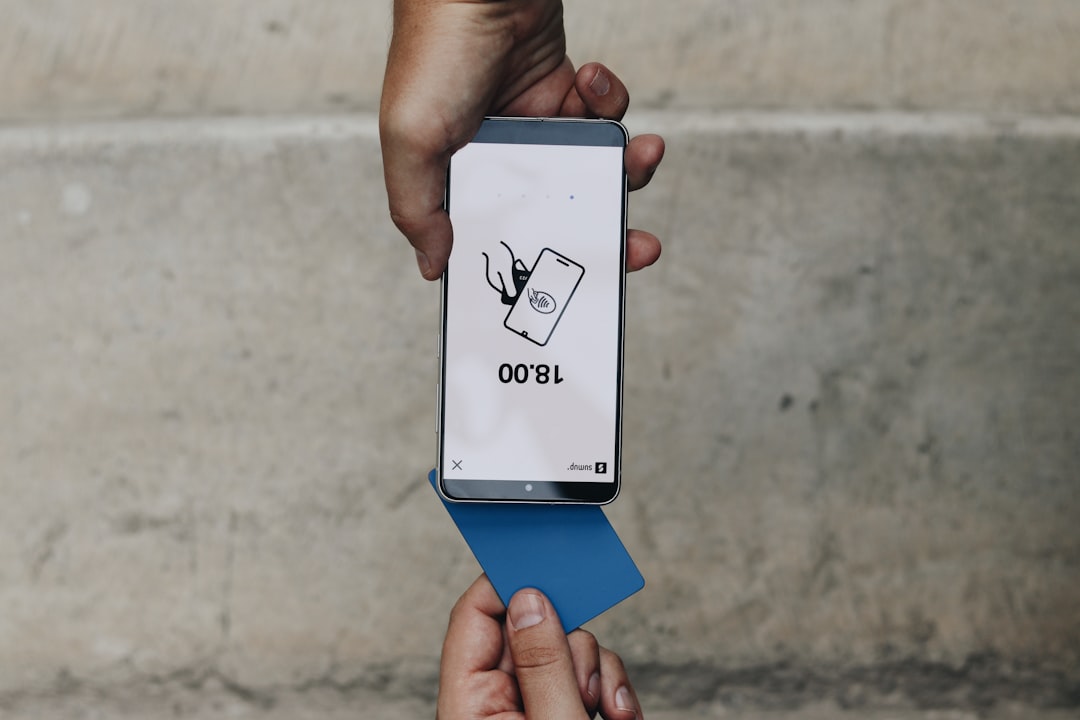 mobile-02 A person holding a smartphone using the Tap to Pay feature with a blue card. The screen displays the amount of 18.00, highlighting the fast and easy mobile payment experience.